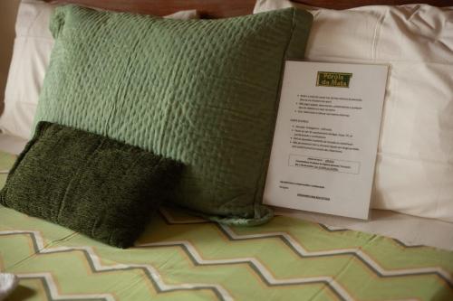 a green pillow and a book on a bed at Pérola da Mata in Boicucanga
