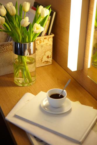 a cup of coffee on a table with a vase of flowers at Aegli Hotel Volos in Volos
