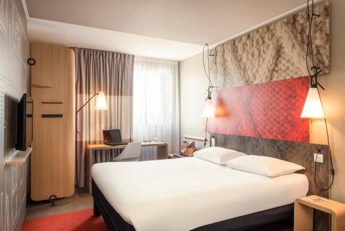 a hotel room with a large white bed and a desk at Ibis Paris Gare Montparnasse 15ème in Paris