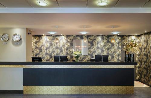 a lobby with a reception desk with chairs and a wall at Leonardo Hotel Hamburg City Nord in Hamburg