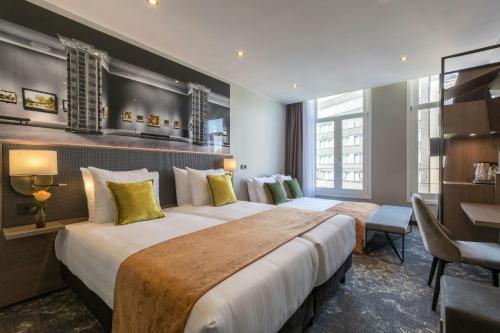 a hotel room with two beds and a desk at Leonardo Hotel Amsterdam Museum Quarter in Amsterdam
