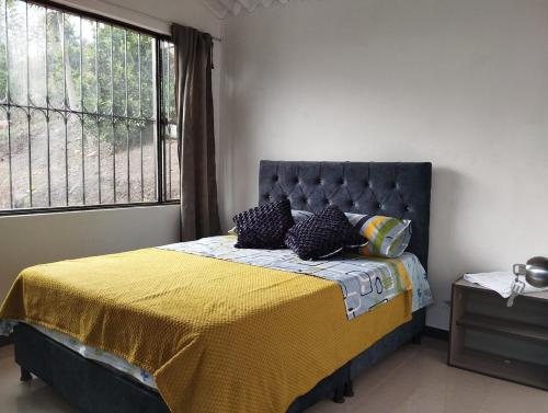 a bedroom with a bed with a yellow blanket and a window at Mi Cabaña in Nimaima