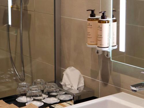 a bathroom with two bottles and glasses and a sink at Hôtel Mercure Rochefort La Corderie Royale in Rochefort
