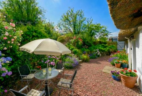 a table and chairs with an umbrella in a garden at Thatched Cottage on Northumberland border in Kirk Yetholm