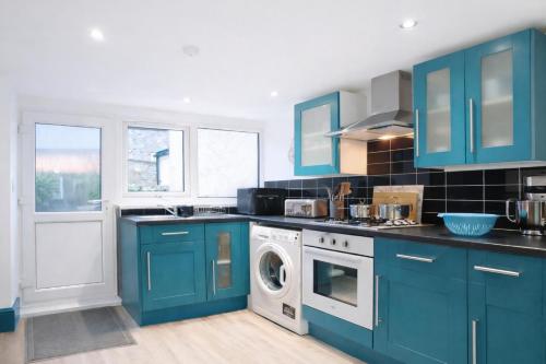 a kitchen with blue cabinets and a washing machine at Walk to Town, Parking, Family Home, drive to beach in Bridgend