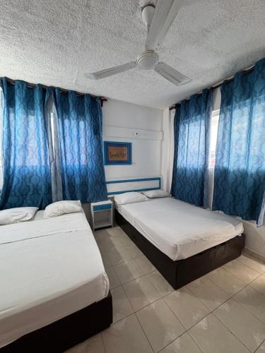 two beds in a room with blue curtains at Acapulco LUUM hotel in Acapulco