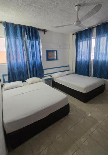 two beds in a room with blue curtains at Acapulco LUUM hotel in Acapulco