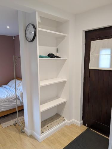 a room with white shelves and a clock on the wall at Studio Apartment - Iver Heath in Uxbridge