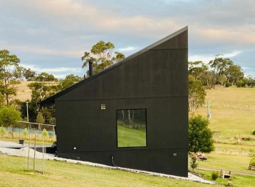 a black house with a large window at Architecturally Designed Rural Retreat 3 bedroom HOUSE or 1 bedroom CABIN with more than 150 five stars rating in Forcett