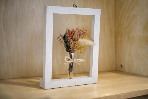 a vase with flowers in a white frame on a table at Fierement inn in Sapporo