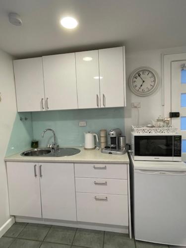 a kitchen with white cabinets and a clock on the wall at Salty Kisses in Narrabeen