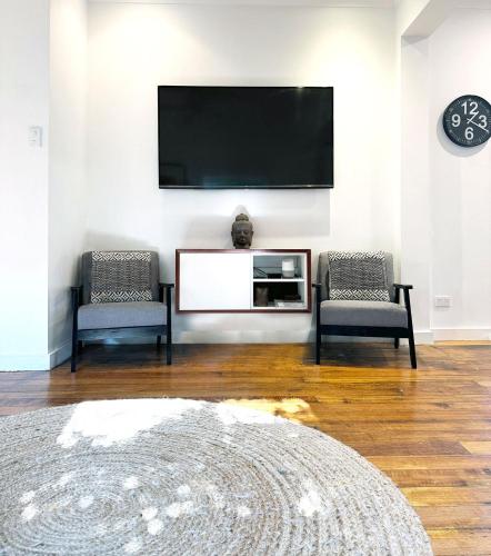 a living room with two chairs and a flat screen tv at Welcome to The Roy - Family home close to airport and train! in Melbourne