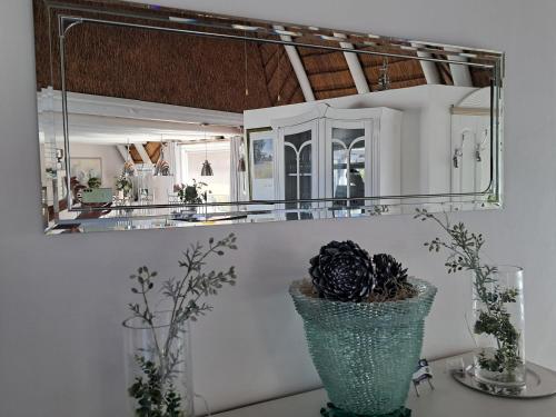 a mirror on a wall above a vase with a plant at Beach Style Cottage in Langebaan