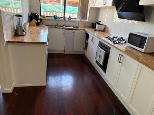 a kitchen with white cabinets and a wooden floor at Budget rooms in big house in Kelmscott