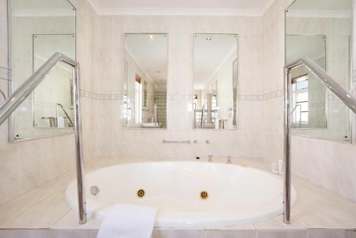 a bathroom with a tub and two mirrors at Cumberland Hotel & Conference Centre Worcester in Worcester