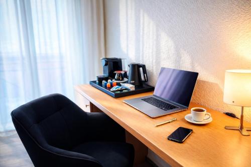 a desk with a laptop and a cup of coffee on it at The Business Loft in Wolfsburg