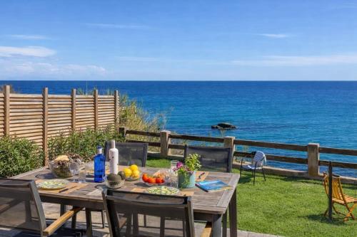 un tavolo e sedie in legno con l'oceano sullo sfondo di Villa Erbalunga a Erbalunga