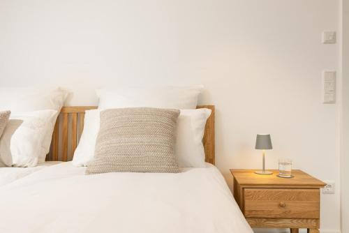 a white bed with white pillows and a wooden night stand at Chiemsee Apartment 17 in Übersee