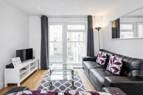 a living room with a black leather couch and a tv at Roomspace Serviced Apartments - Abbot's Yard in Guildford