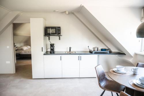 a kitchen with white cabinets and a table and a bed at Sfeervol appartement voor 2 personen De Jonge Blomme in Kamperland