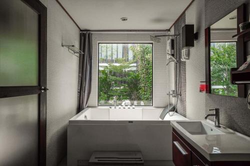 a bathroom with a tub and a sink and a window at The Grace Amphawa in Amphawa