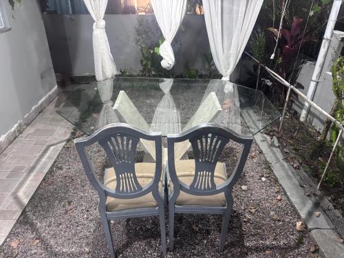 a glass table with two chairs in front of a window at Casa aconchegante in Palhoça
