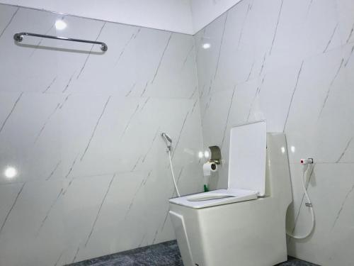 a white bathroom with a toilet and a white wall at Diyana Cottage in Sigiriya