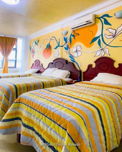 two beds in a hotel room with a painting on the wall at Hotel Delfin Rosado in Puyo