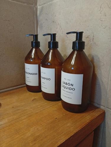 three bottles of liquid sitting on a wooden shelf at Casa Boreal dptos estilo casa in Puerto Madryn