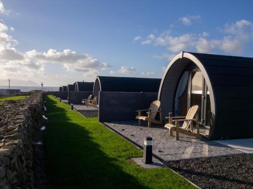 a building with a stone wall and chairs next to a yard at Bayview Glamping Pods Kerry in Ballyheigue