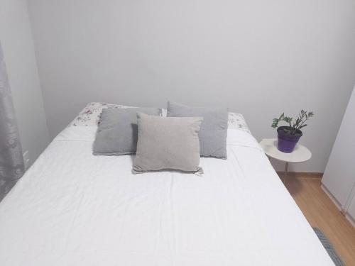 a white bed with gray pillows and a plant on it at Juhh Bella in Botucatu