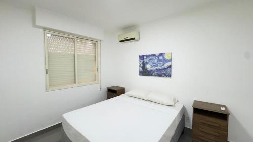 a white bedroom with a bed and a window at Edifício Aquarius in Ribeirão Preto