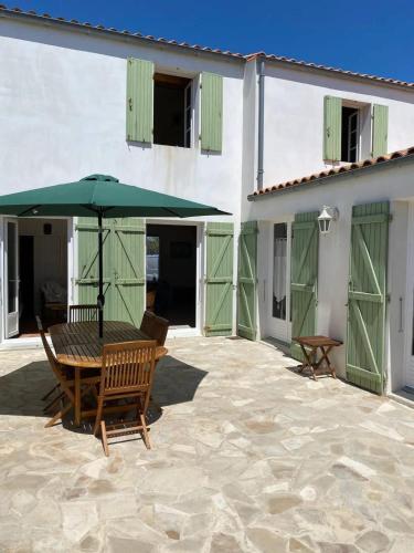 a patio with a wooden table and an umbrella at La Villa de la Digue in Saint-Clément-des-Baleines