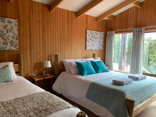 two beds in a bedroom with wooden walls and a window at Lodge Cumbres de Chiloe in Castro