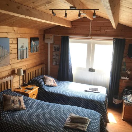two beds in a room with wooden walls at Weston's Wood Cabins in Blakeney