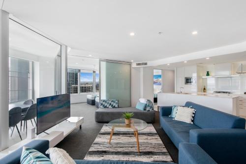 a living room with blue couches and a kitchen at Q Tower Apartments - Hosted by Wow Stay in Gold Coast