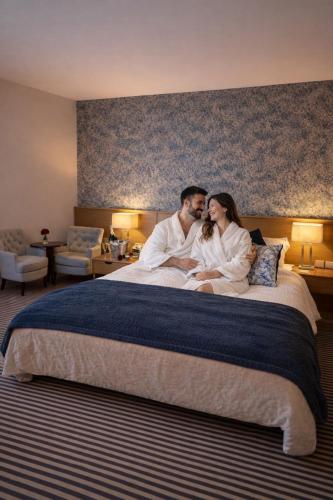 a man and a woman sitting on a bed at The Hedges Hotel in Stranocum