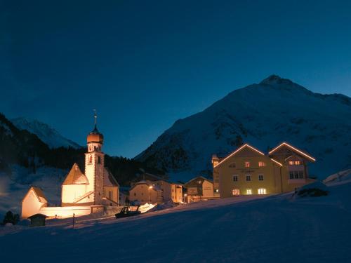 a building with a clock tower in front of a mountain at first mountain Hotel Ötztal in Längenfeld