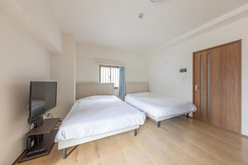 a room with two beds and a tv and a door at Jintai House201 in Fukuoka