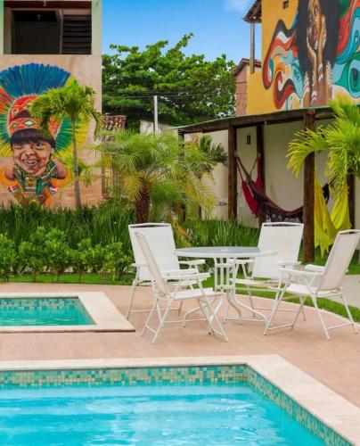 a pool with chairs and a table and a mural at Condomínio Diver in Vera Cruz de Itaparica