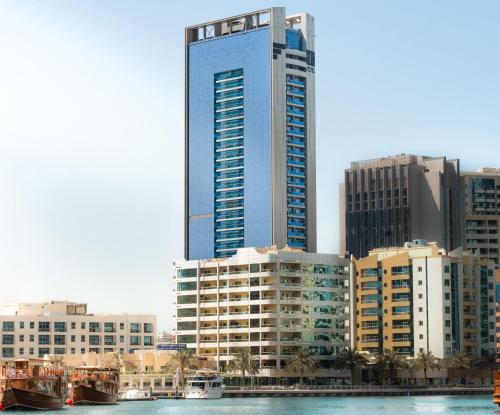 a tall blue building next to a river with buildings at The First Collection Marina, Dubai, a Tribute Portfolio Hotel in Dubai