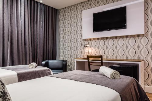 a hotel room with two beds and a tv on the wall at Vogue Hotel Rio in São João de Meriti