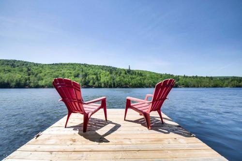 two red chairs sitting on a dock on a lake at Lakefront - Chalet Le Missionnaire in Trois Rives