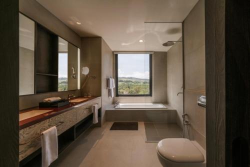 a bathroom with a tub and a toilet and a window at Nawana Sentul City by Alana in Bogor