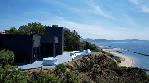 a black house on a hill next to the ocean at eureka awaji 絶景インフィニティプール x 露天温水ジャグジー付きヴィラ in Sumoto