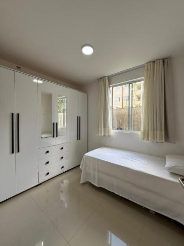 a white bedroom with a large bed and a window at AP da FLOR Guerra in Parnamirim