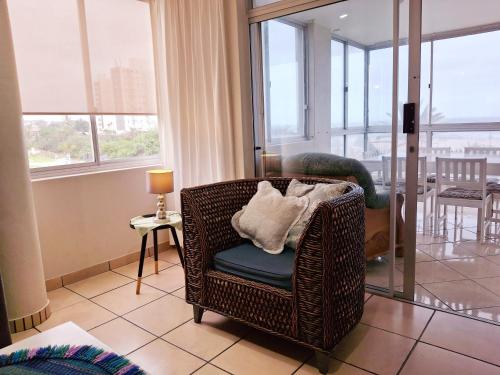a wicker chair sitting in a room with windows at Margate Boulevard Beachfront Apartment in Margate