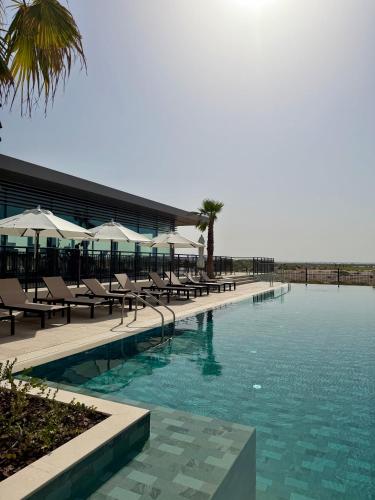 a swimming pool with chairs and umbrellas next to a building at Elegant Studio apartment in Yas Golf collection with Balcony and Free parking l Near Yas water world & Ferrari World & Warner brothers in Abu Dhabi