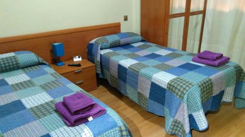 ログローニョにあるペンシオン カルフレッド Ⅱのホテルルーム内のベッド2台(紫色のタオル付)