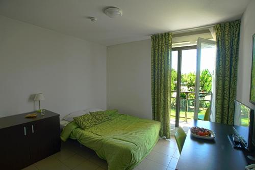1 dormitorio con cama verde y balcón en KOSY Appart'Hôtels - Campus Del Sol Esplanade, en Montfavet